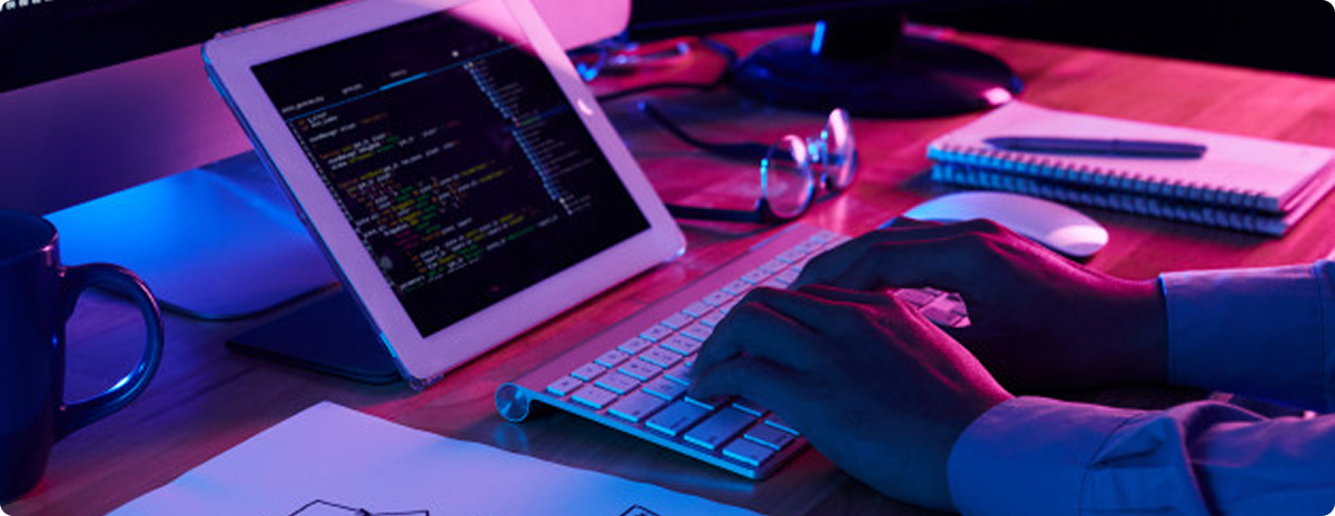 Developer workspace with keyboard, tablet, and code under colored lighting